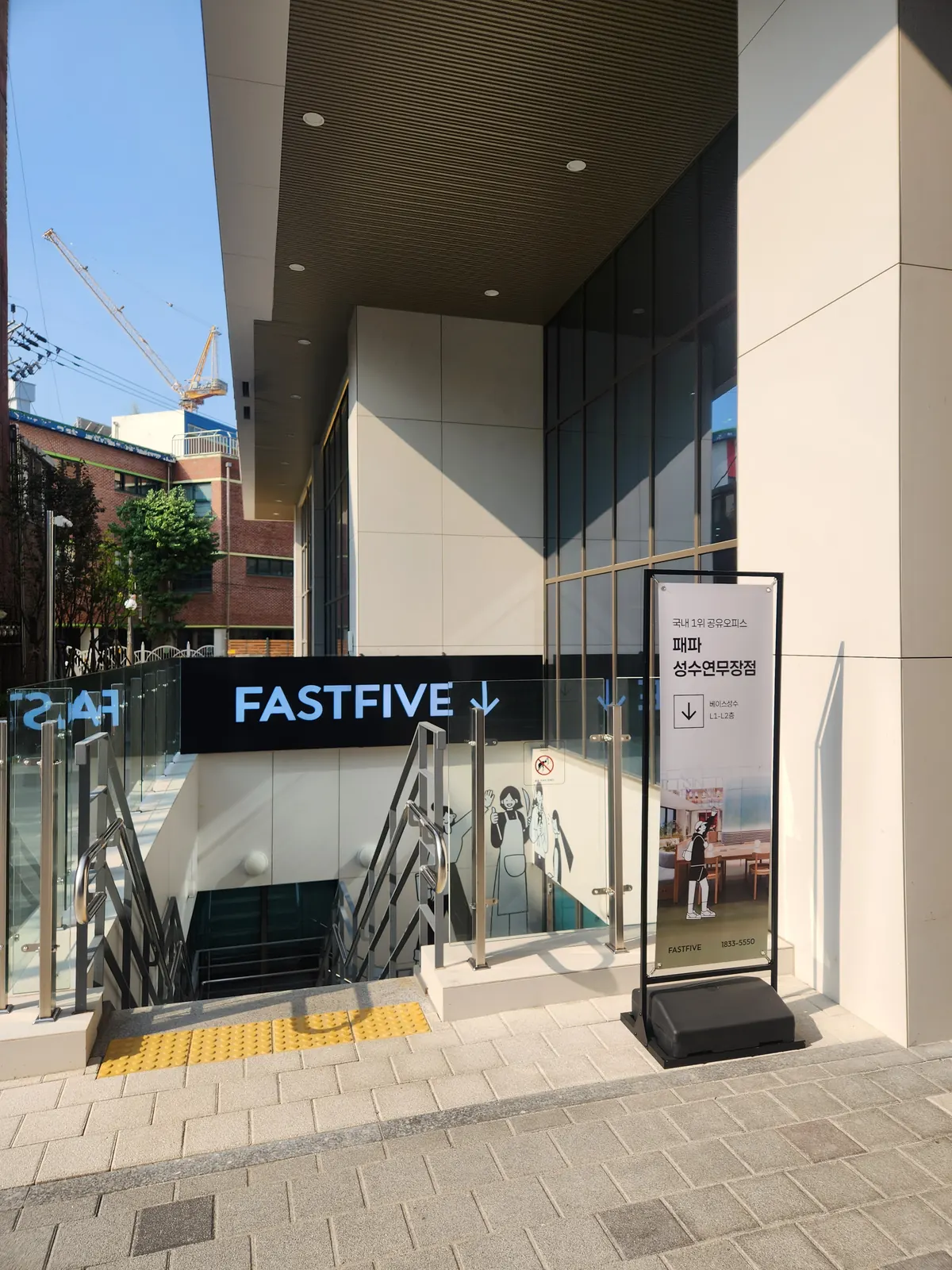 건물 옆 계단 입구. 'FASTFIVE ↓' 간판 아래 '패파 성수연무장점, 베이스성수 L1-L2층' 입간판이 서 있다